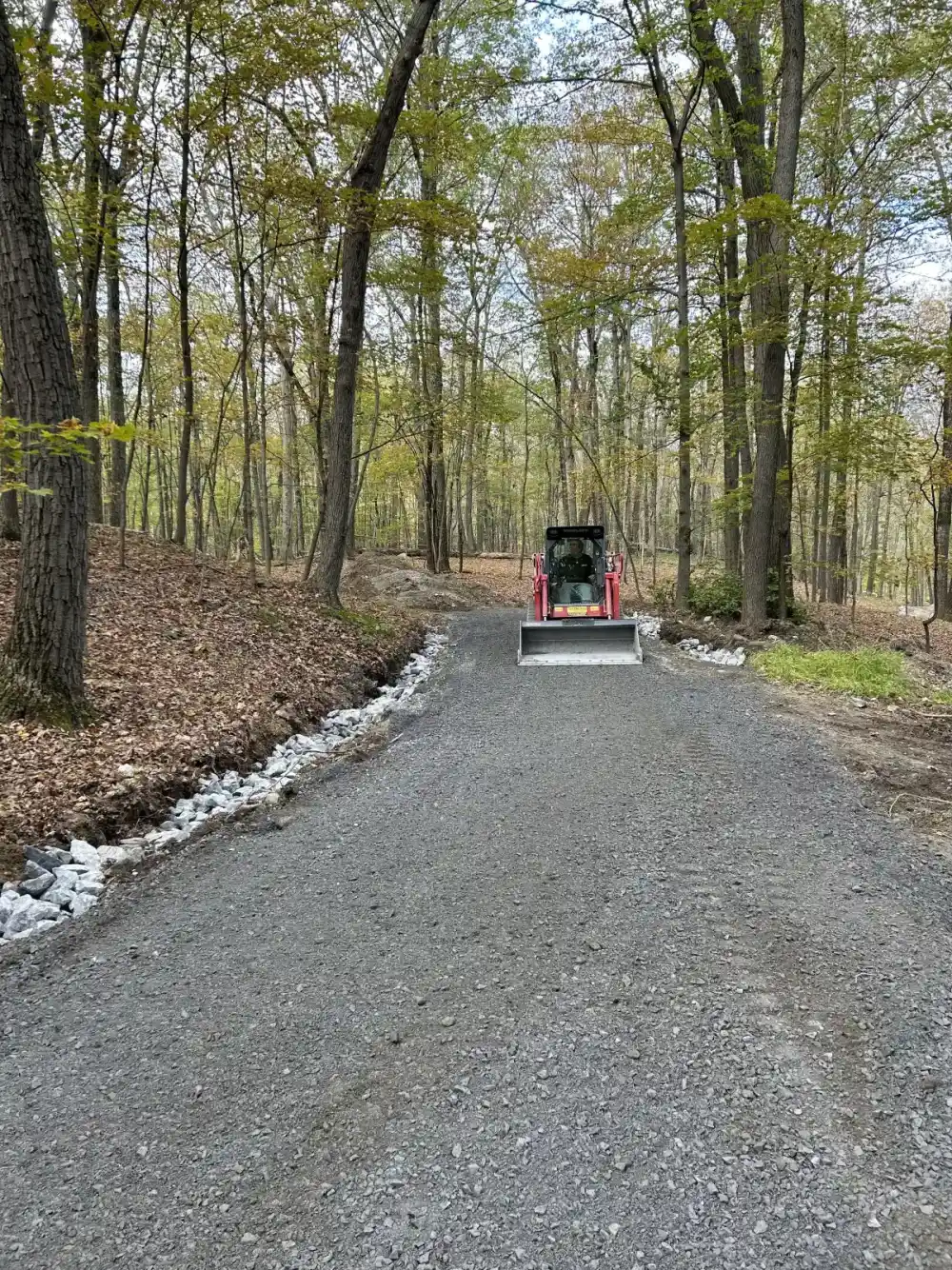 Tractor grading a fresh gravel driveway through wooded property in Dutchess County